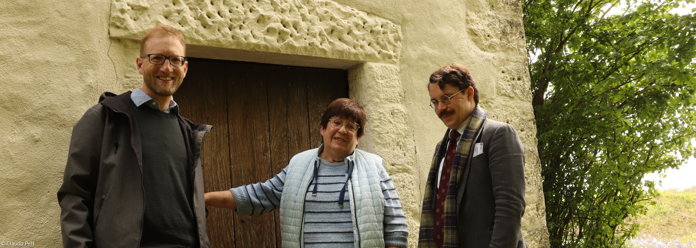 Dekan Max von Egidy gemeinsam mit Angelika Arlt und Pfarrer Marvin Askani vor der kleinsten Kirche im Dekanat Uffenheim. Sie ist wie alle 43 Kirchen am Tag der offenen Kirchen am Pfingstmontag, 25.5.26 geöffnet