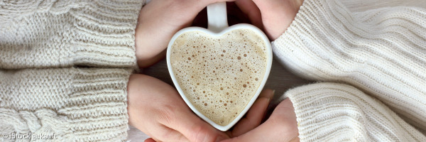 Zwei Hände umfassen eine Herztasse mit Kaffee