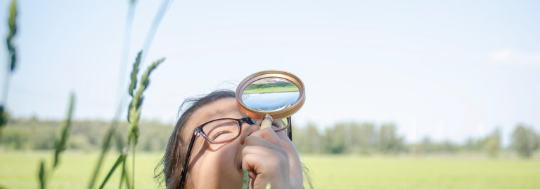 Kind schaut durch eine Lupe in den Himmel