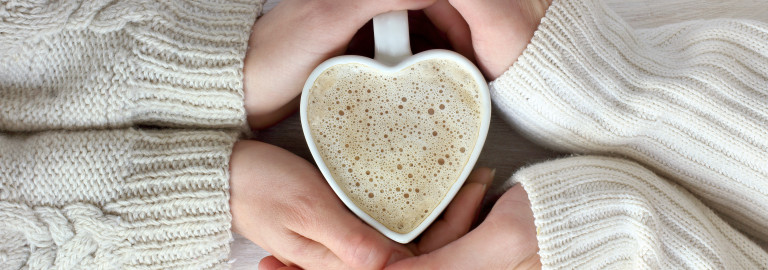 Zwei Hände umfassen eine Herztasse mit Kaffee